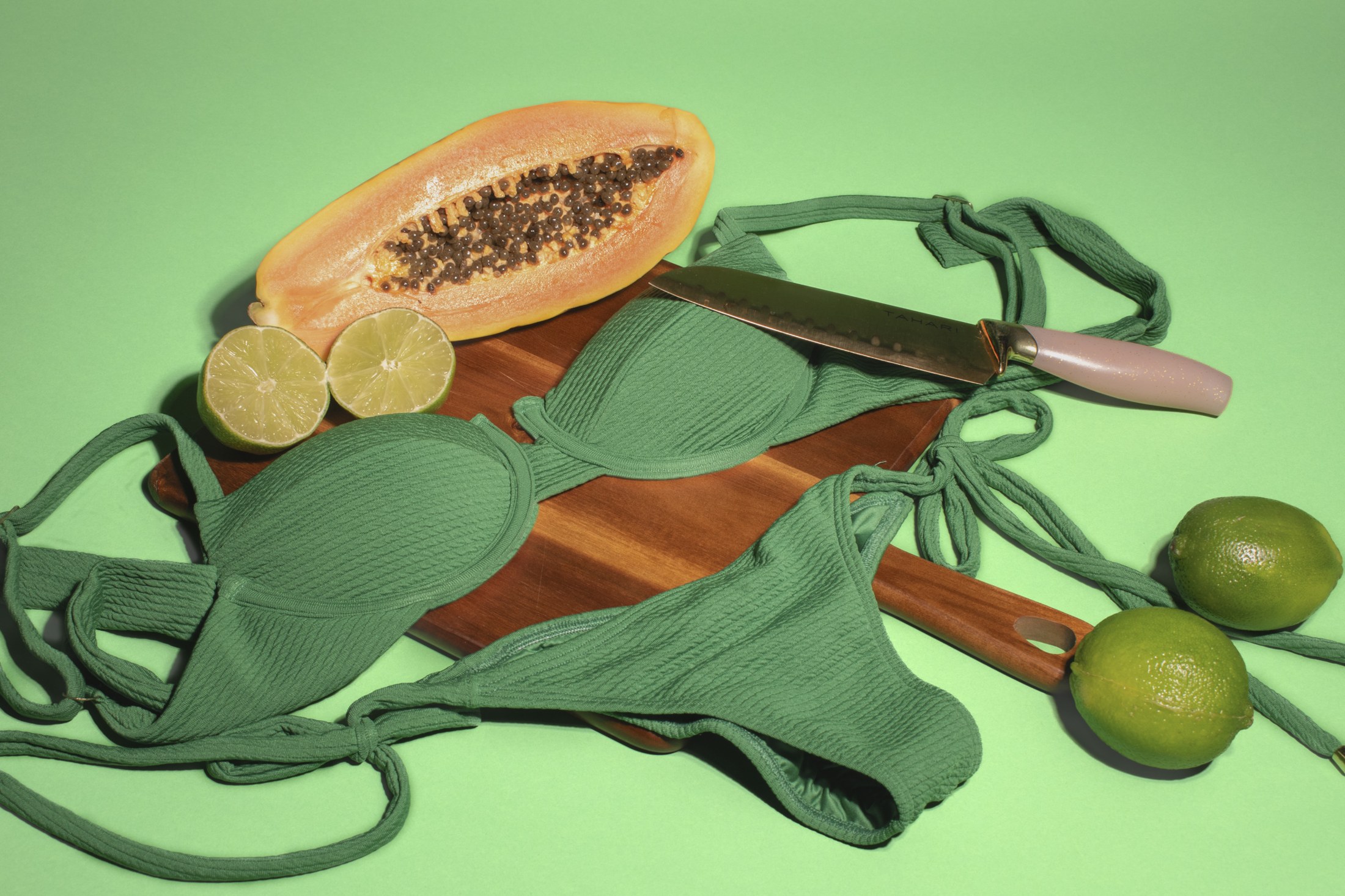 Green Merci Solei swimwear with papaya on a tonal backdrop